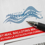 Vote-by-mail envelope with pen on top.
