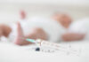 A syringe placed on a surface with a blurred baby in the background