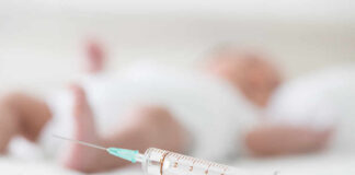A syringe placed on a surface with a blurred baby in the background