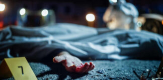 Crime scene with covered body and hand exposed.
