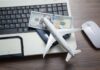 Airfare EXPLOSION Crushing Travelers A model airplane on a laptop keyboard with a passport and cash