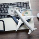 A model airplane on a laptop keyboard with a passport and cash