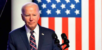 Joe Biden speaking at a podium with US flag background.