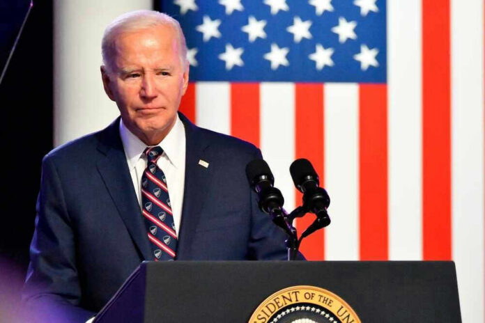 Joe Biden speaking at a podium with US flag background.