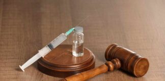 A syringe and a vial placed next to a wooden gavel on a table