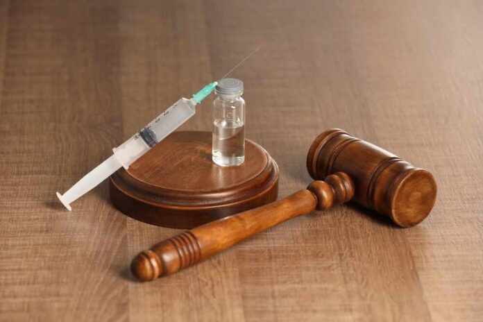 A syringe and a vial placed next to a wooden gavel on a table