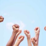Multiple raised fists against a blue sky