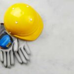 Yellow hard hat, measuring tape, and gloves on a gray surface