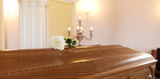 A wooden casket with a white rose placed on top in a solemn setting