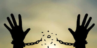 Silhouetted hands breaking chains against sunset sky.