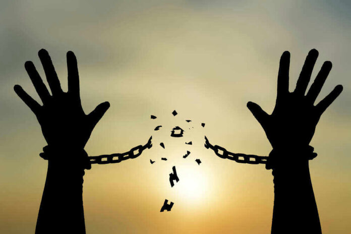 Silhouetted hands breaking chains against sunset sky.