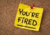 A yellow sticky note pinned to a corkboard with the words 'YOU'RE FIRED' written on it