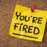 A yellow sticky note pinned to a corkboard with the words 'YOU'RE FIRED' written on it