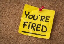 A yellow sticky note pinned to a corkboard with the words 'YOU'RE FIRED' written on it