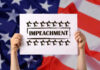 Hands holding impeachment sign over American flag.