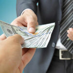 A person handing over a stack of cash to another individual in a suit