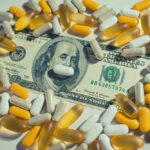 A one hundred dollar bill surrounded by various capsules and pills