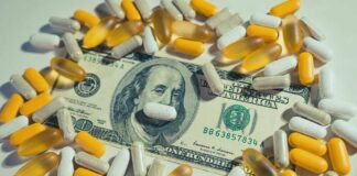 A one hundred dollar bill surrounded by various capsules and pills