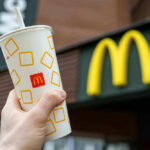 Hand holding McDonalds cup in front of restaurant sign.