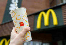 Hand holding McDonalds cup in front of restaurant sign.