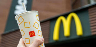 Hand holding McDonalds cup in front of restaurant sign.