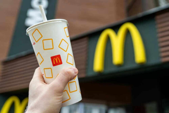 Hand holding McDonalds cup in front of restaurant sign.