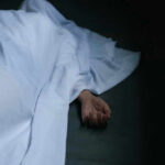 Hand emerging from under white sheet on dark surface.