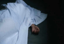 Hand emerging from under white sheet on dark surface.