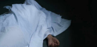 Hand emerging from under white sheet on dark surface.