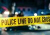 Police line caution tape at a crime scene with blurred figures in the background