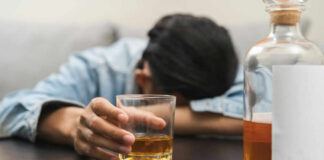 Person asleep at table holding drink glass