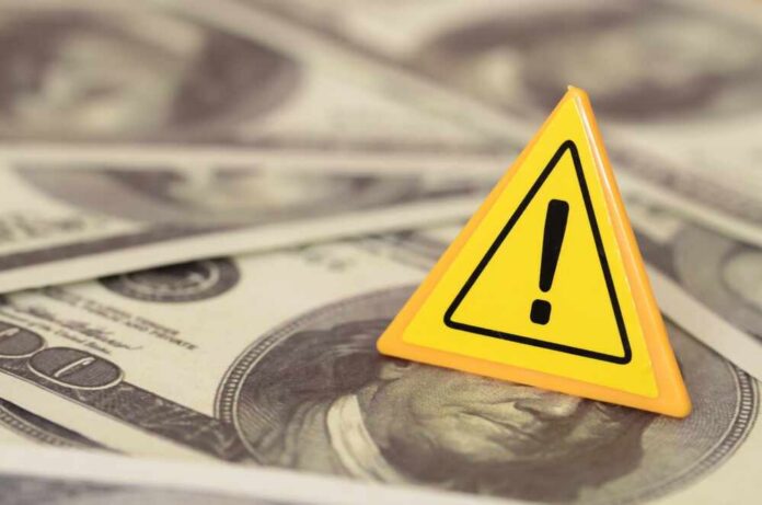 shutterstock_2513395725.jpg A yellow warning sign on a background of dollar bills