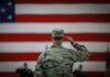 Automatic Military Draft Registration Begins This Year A military personnel saluting in front of a large American flag