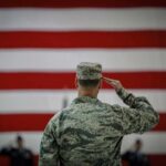 A military personnel saluting in front of a large American flag