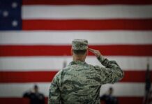 A military personnel saluting in front of a large American flag