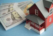 A model red house next to stacks of hundred-dollar bills