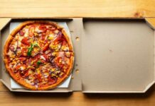 A pizza with various toppings in an open pizza box on a wooden table