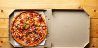 A pizza with various toppings in an open pizza box on a wooden table