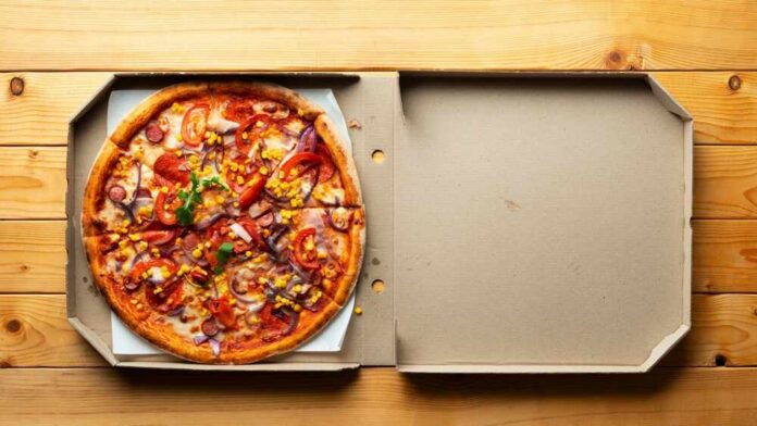 A pizza with various toppings in an open pizza box on a wooden table