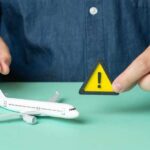 Iran War DOUBLES Fuel — Airlines Cut Major Routes A person holding a warning sign next to a model airplane