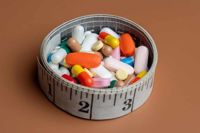 A bowl filled with various colorful pills and capsules next to a measuring tape