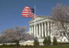 U.S. Supreme Court building with an American flag and cherry blossom trees
