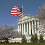 U.S. Supreme Court building with an American flag and cherry blossom trees
