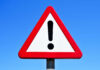 A triangular warning sign with an exclamation mark against a blue sky