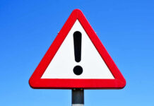 A triangular warning sign with an exclamation mark against a blue sky