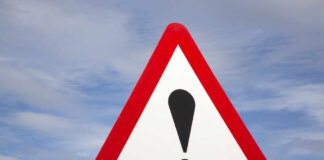 A triangular warning sign with an exclamation mark against a blue sky