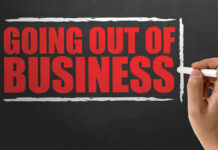 A hand writing 'GOING OUT OF BUSINESS' on a chalkboard