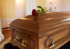 A wooden casket with a red rose placed on top
