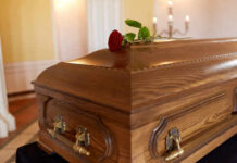 A wooden casket with a red rose placed on top