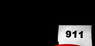 A red telephone next to a sign displaying the number 911 on a dark background